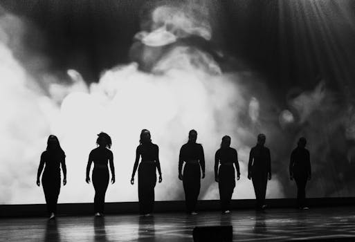 Silhouette de danseurs en noir sur scène, avec un fond lumineux et brumeux, illustrant une performance artistique.