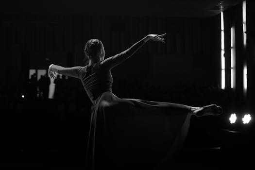 Danseuse en silhouette exécutant un mouvement gracieux sur scène, éclairée par des projecteurs.