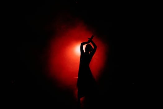 Silhouette d'un danseur en mouvement, éclairée par une lumière rouge dans une ambiance sombre.