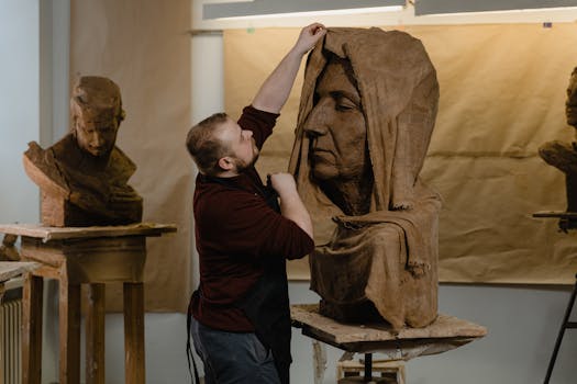 Artiste travaillant sur une sculpture en argile d'un visage féminin, dans un atelier avec d'autres bustes en arrière-plan.